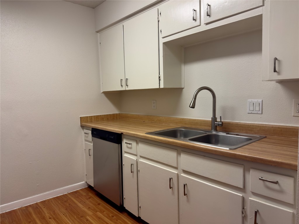 115 Waller Street, Unit A Austin, TX 78702 - Photo 4 of 18 Kitchen featuring light countertops, light wood-type flooring, stainless steel dishwasher, white cabinetry, and a textured wall