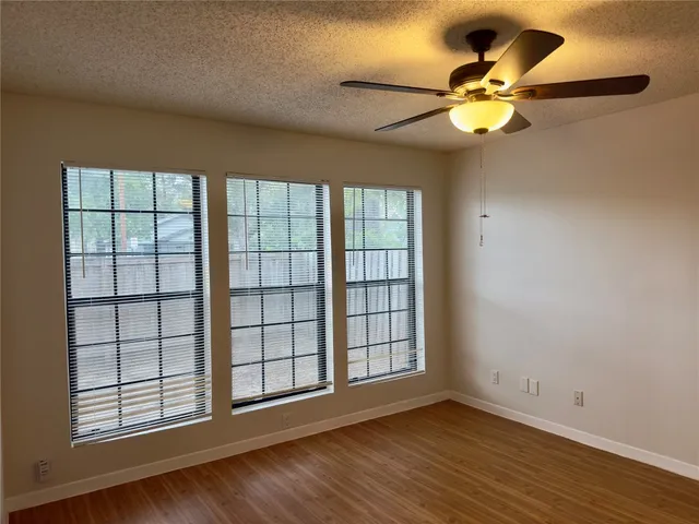 an empty room with wooden floor fan and windows