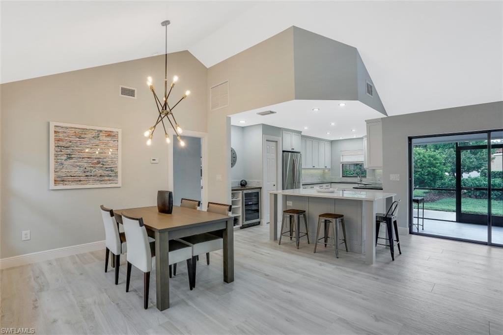 714 Reef Point Circle Naples, FL 34108 - Photo 3 of 27 a dining room with wooden floor a chandelier a wooden table and chairs