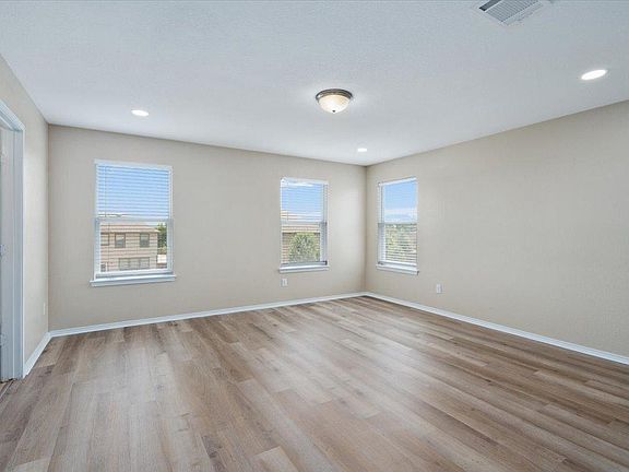 904 Lonesome Lilly Way Pflugerville, TX 78660 - Photo 20 of 34 The room features light wood-style flooring, three windows with blinds, and recessed lighting in the ceiling, complemented by a central flush-mount light fixture