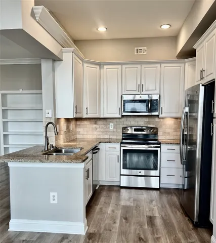 a kitchen with stainless steel appliances granite countertop a stove top oven a sink and dishwasher a refrigerator with wooden floors