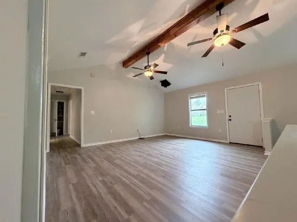 an empty room with wooden floor chandelier fan and windows