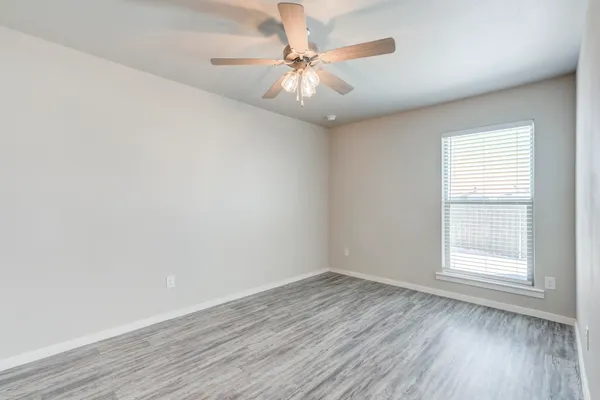an empty room with wooden floor chandelier fan and windows