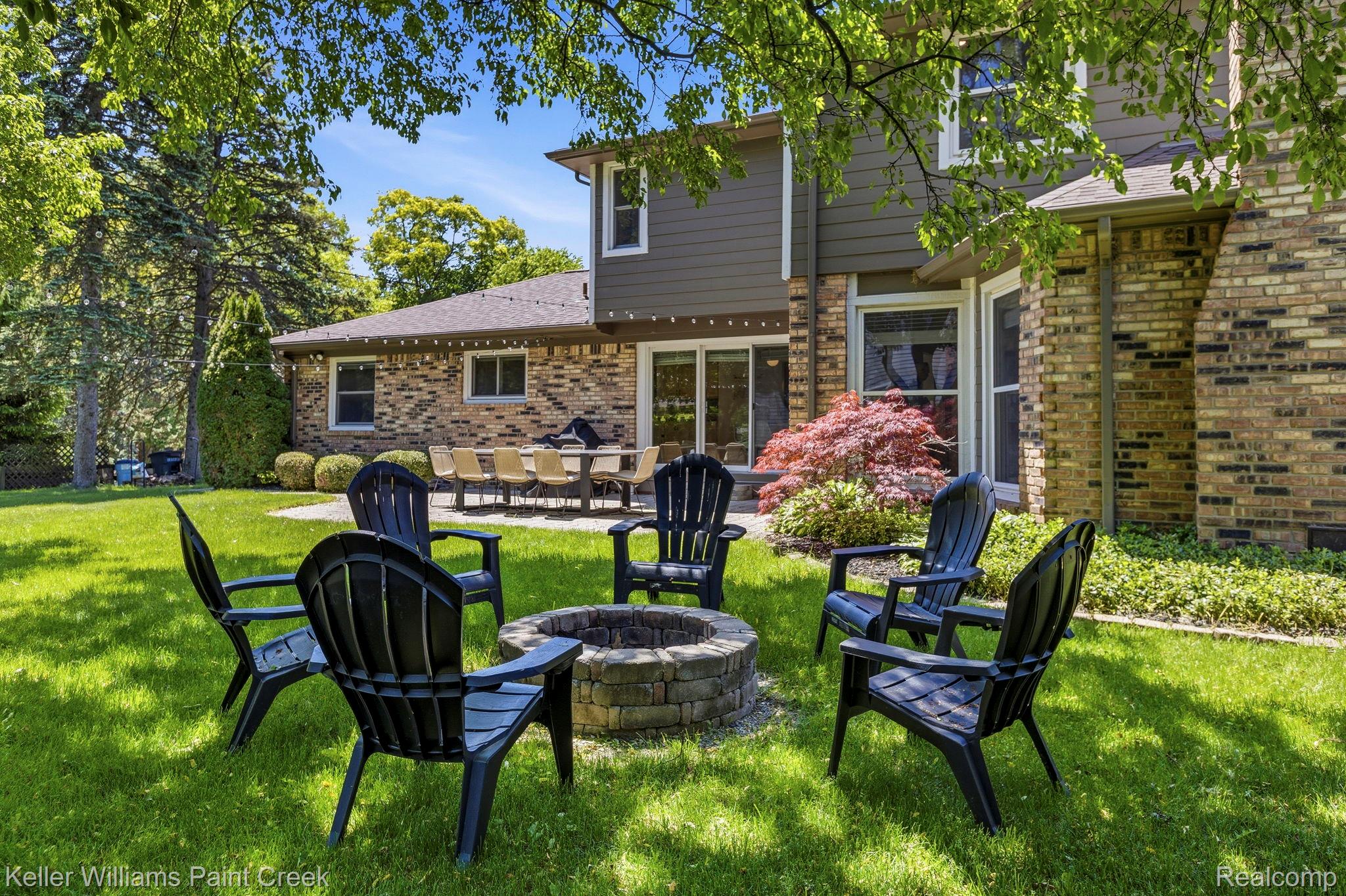 1675 North Kilburn Road Rochester, MI 48306 - Photo 8 of 48 Expansive backyard featuring a stone-clad fire pit, mature trees, a multi-pane sliding glass door, and a brick and siding exterior