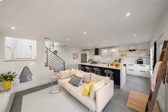 a living room with stainless steel appliances furniture a rug and a kitchen view