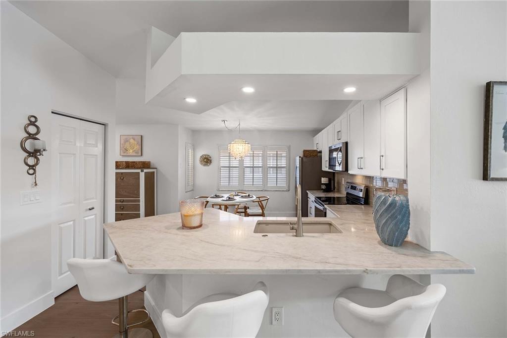 2450 Old Groves Road, Unit 201 Naples, FL 34109 - Photo 8 of 32 a kitchen with stainless steel appliances kitchen island granite countertop a table chairs and a refrigerator