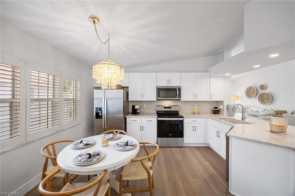 2450 Old Groves Road, Unit 201 Naples, FL 34109 - Photo 10 of 32 a kitchen with stainless steel appliances granite countertop a stove a kitchen island a dining table and chairs with wooden floor