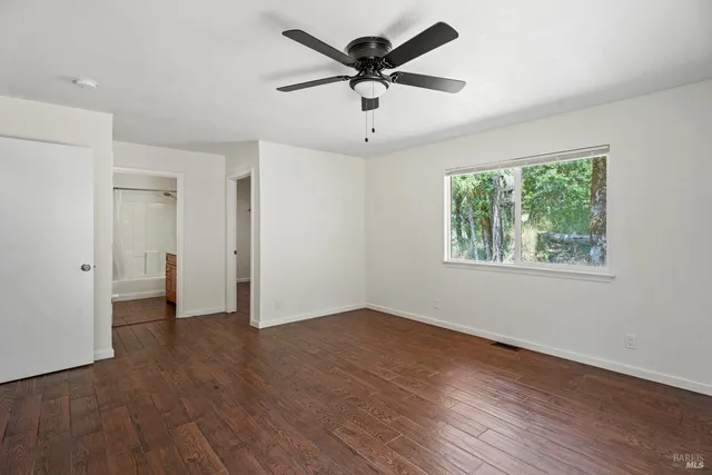 an empty room with wooden floor chandelier fan and windows