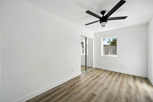 an empty room with wooden floor ceiling fan and windows