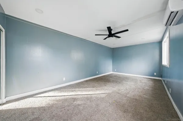 an empty room with chandelier fan and windows