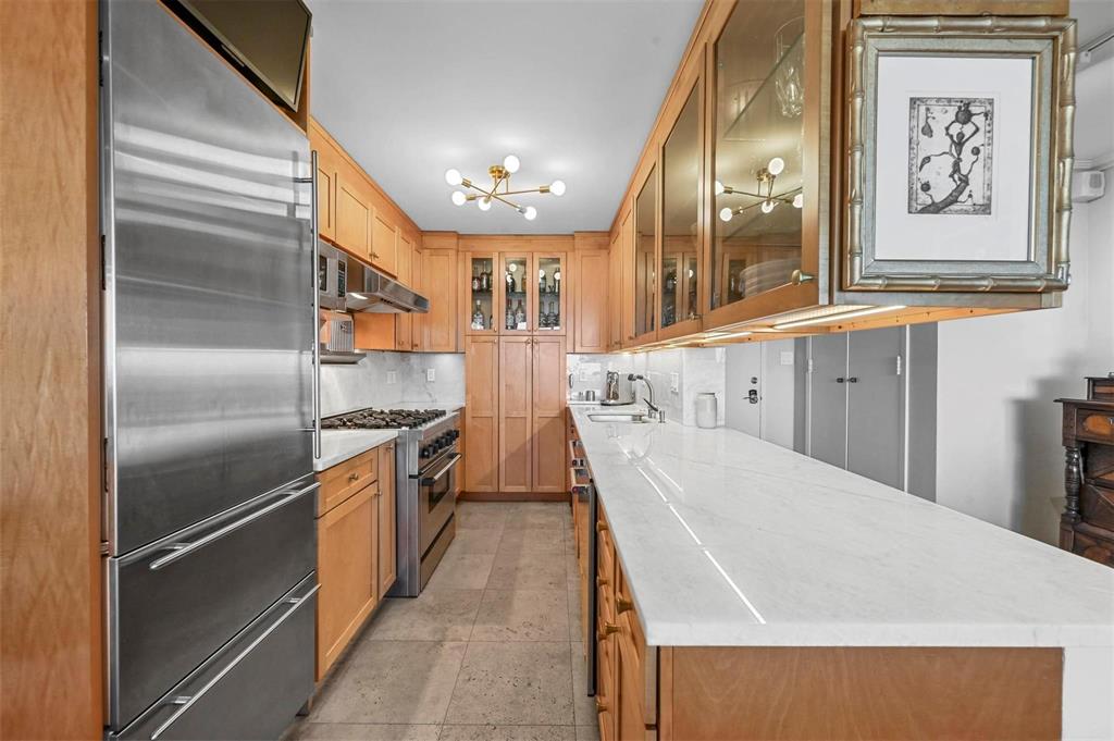 Kitchen with sub zero thermador appliances, tasteful backsplash, light stone counters, glass insert cabinets, and a chandelier