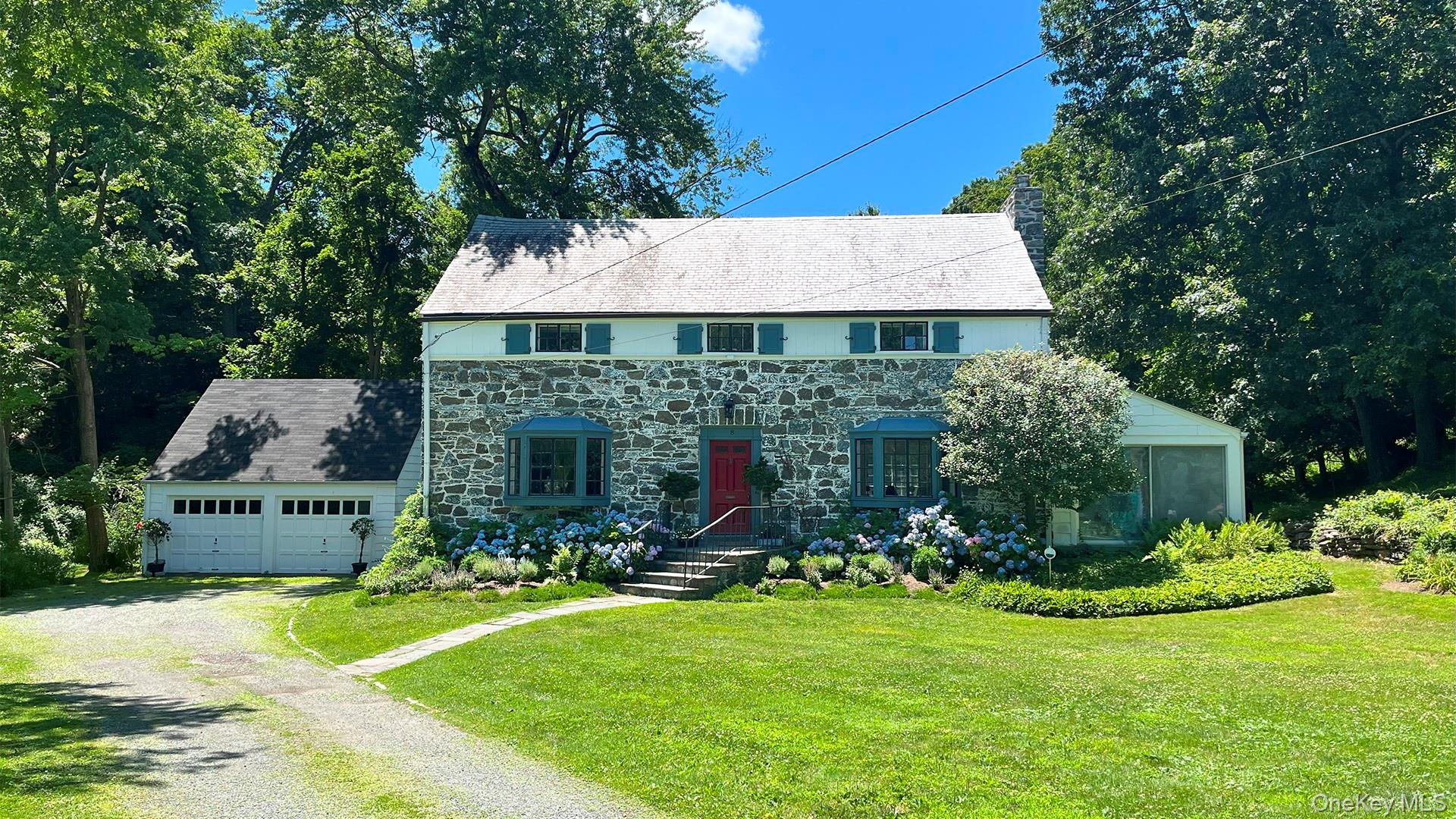 View of front facade with driveway, stone siding, a front lawn, a garage, and a chimney