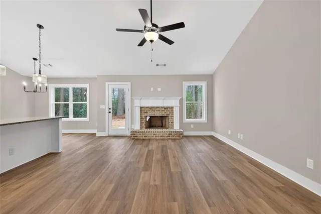 an empty room with wooden floor a ceiling fan a fireplace and windows