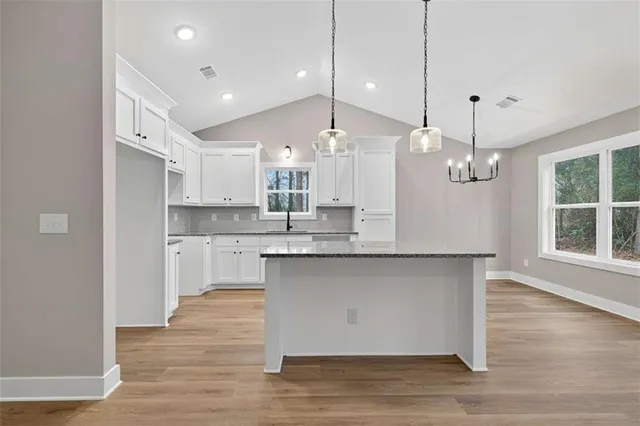a large kitchen with granite countertop a stove a sink and white cabinets with wooden floor