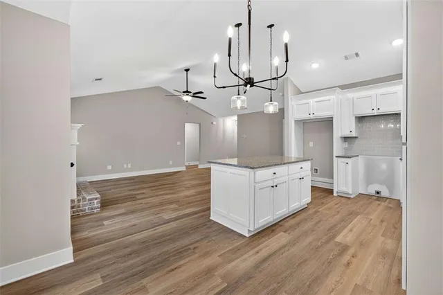 a kitchen with stainless steel appliances granite countertop a stove a sink and white cabinets with wooden floor