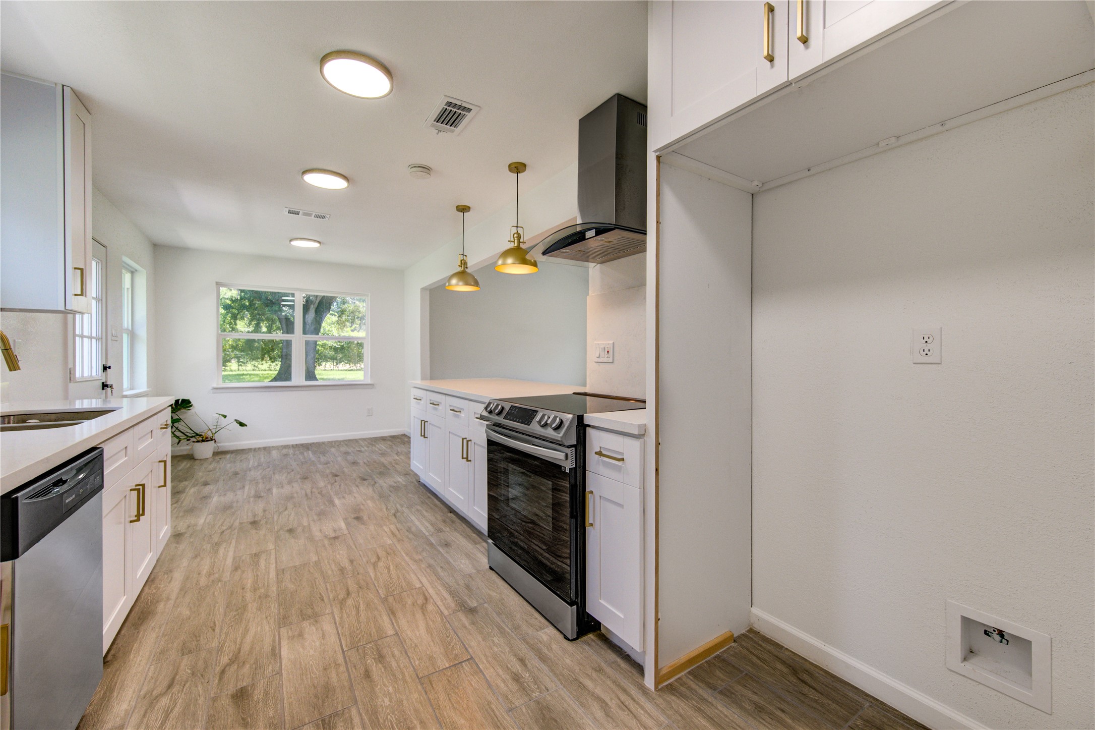 5411 Logston Lane Spring, TX 77389 - Photo 20 of 50 Bright and modern galley kitchen featuring sleek white cabinetry, stainless steel appliances, and elegant pendant lighting, with a large window offering a view of lush greenery.