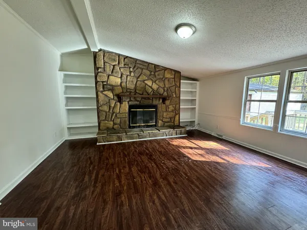 an empty room with wooden floor fireplace and windows
