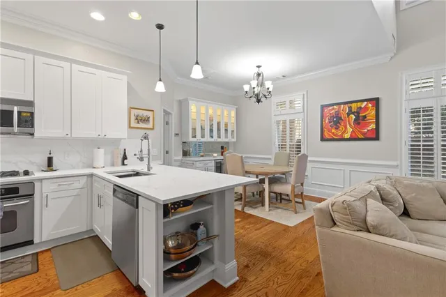 a open kitchen with stainless steel appliances granite countertop a stove top oven a sink dishwasher a dining table and chairs with wooden floor