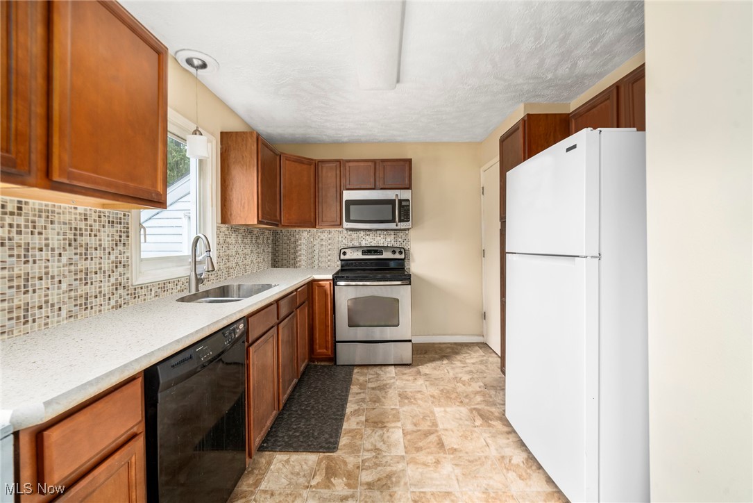 187 Everhard Road Southwest North Canton, OH 44720 - Photo 5 of 19 Kitchen with stainless steel appliances, light countertops, decorative backsplash, brown cabinetry, and hanging light fixtures