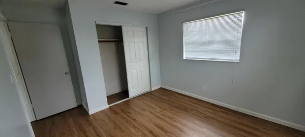 an empty room with wooden floor closet and windows