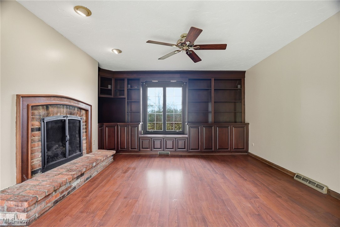 11710 Butternut Road Chardon, OH 44024 - Photo 19 of 48 Unfurnished family room with a brick gas burning fireplace, a ceiling fan, dark wood-type flooring, and built in shelves