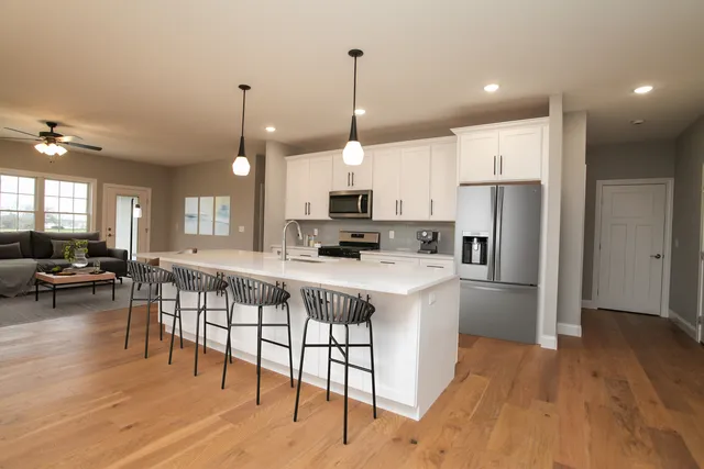 a open kitchen with stainless steel appliances granite countertop a stove a refrigerator a kitchen island a dining table and chairs with wooden floor