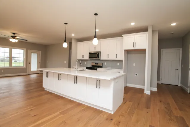 a kitchen with stainless steel appliances granite countertop a stove a sink a refrigerator and white cabinets with wooden floor