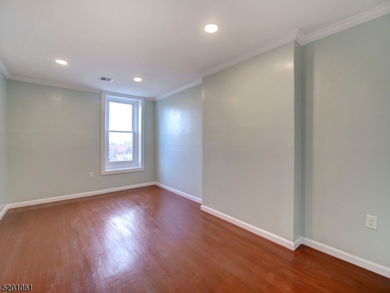 310 Broadway Newark, NJ 07104 - Photo 10 of 11 an empty room with wooden floor and windows with curtains