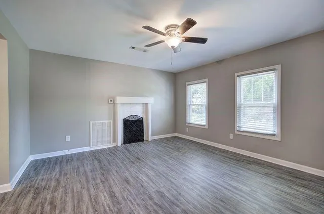 an empty room with chandelier fan and windows