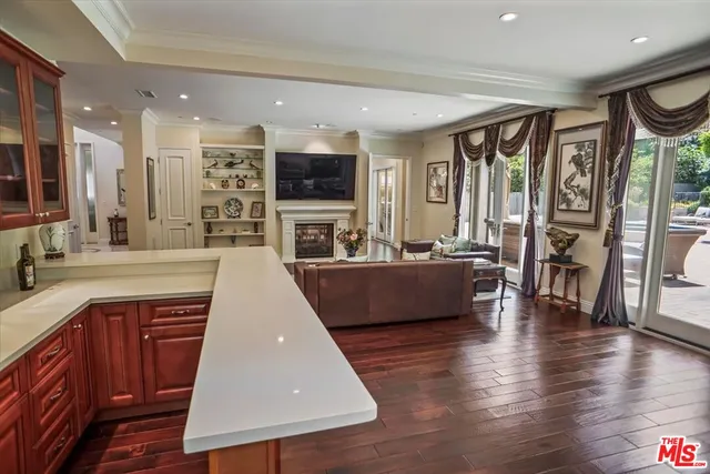 a living room with stainless steel appliances furniture a fireplace a flat screen tv and a large window