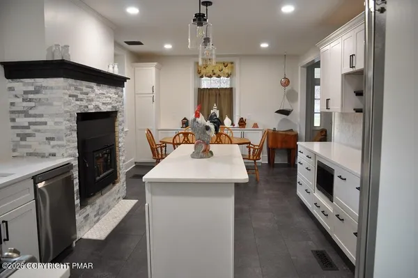 a kitchen with stainless steel appliances kitchen island granite countertop a refrigerator a sink dishwasher and a fireplace with wooden floor