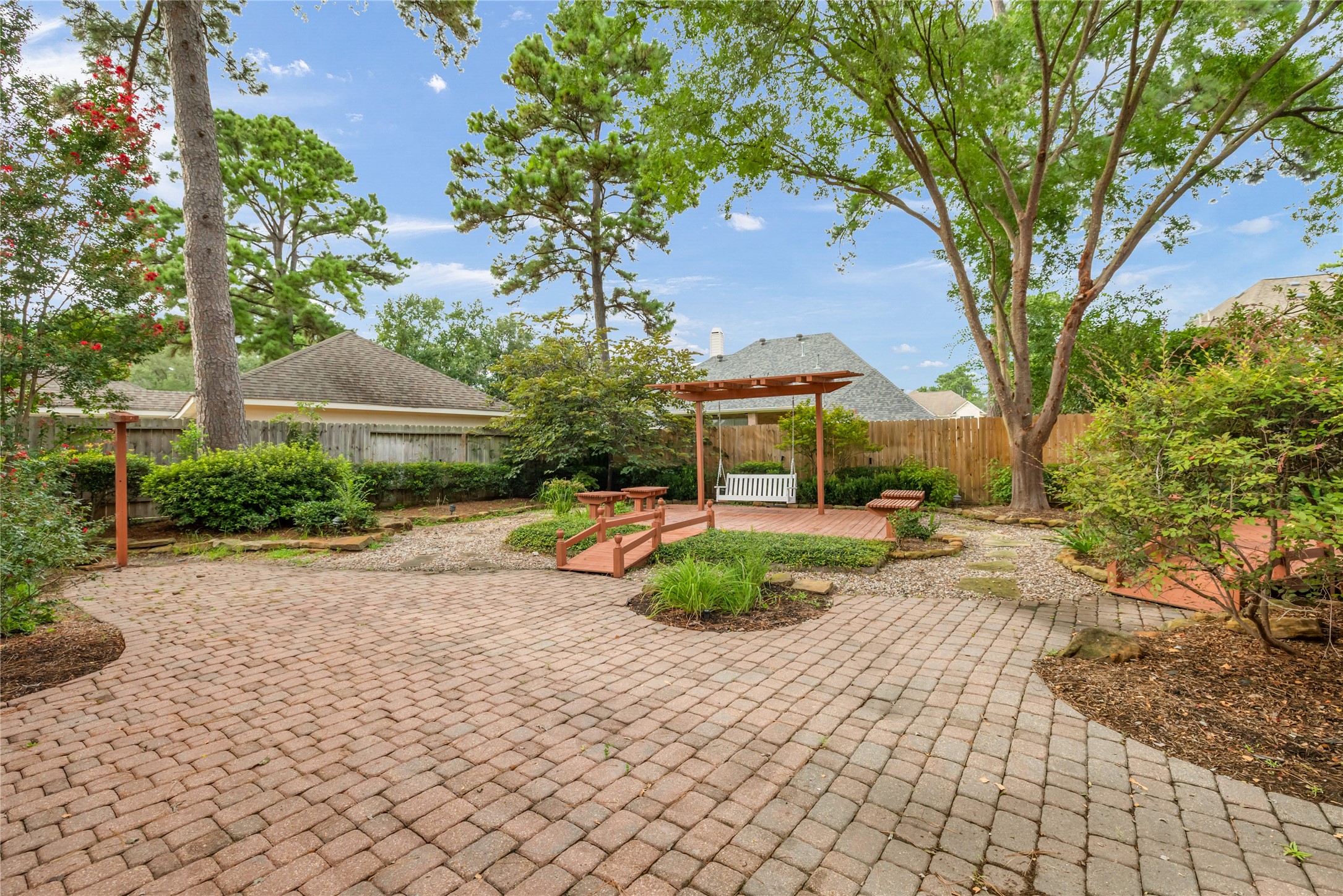 6518 Briarstone Lane Spring, TX 77379 - Photo 36 of 46 Elegantly landscaped, the backyard showcases stone pathways, brick pavers, and mature trees that provide both shade and privacy. A charming wooden pergola with a swing creates a serene outdoor retreat perfect for relaxation.