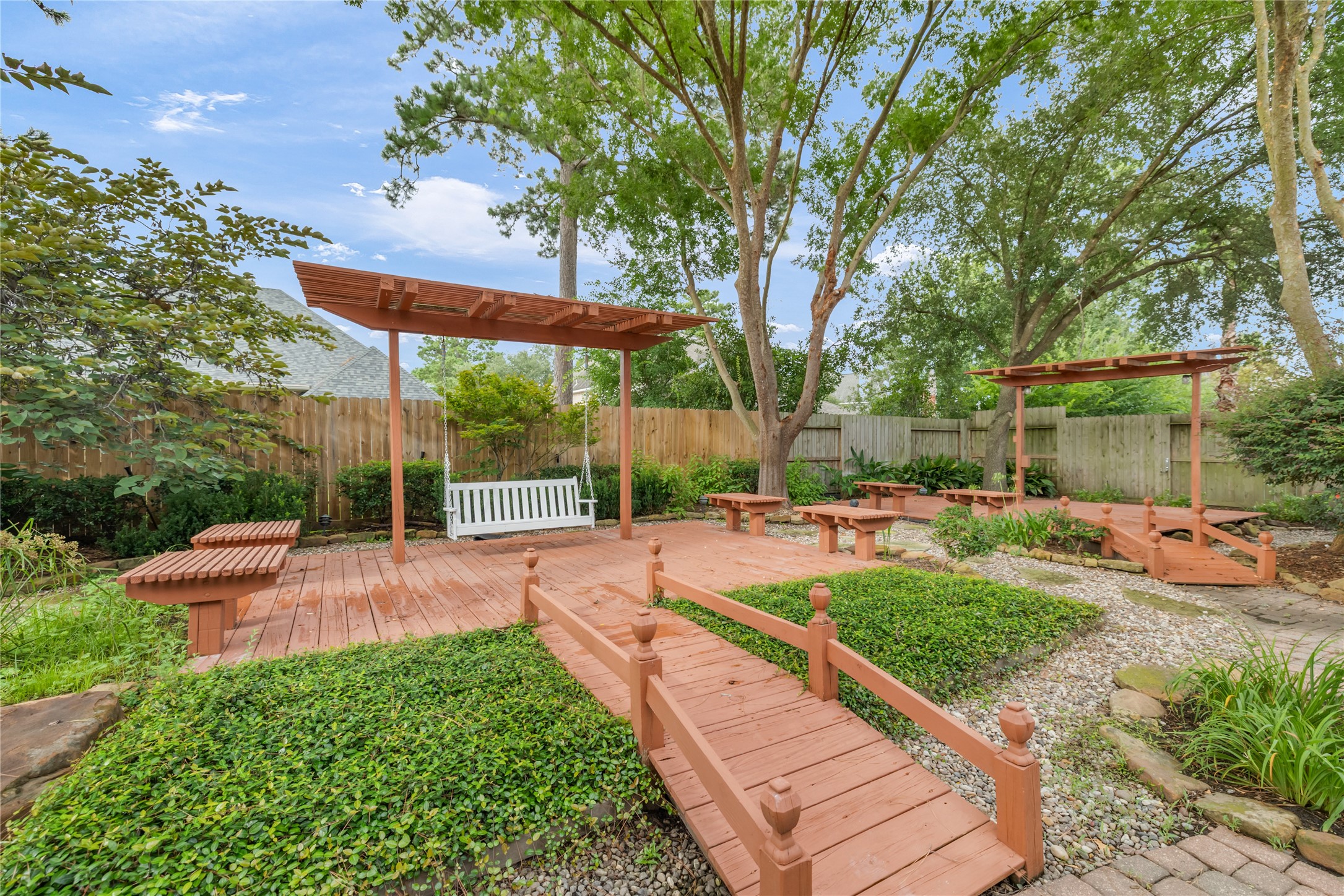 6518 Briarstone Lane Spring, TX 77379 - Photo 38 of 46 The charming pergola-covered swing sits on a raised wooden platform, surrounded by benches, greenery, and gravel walkways—creating a relaxing backyard oasis.
