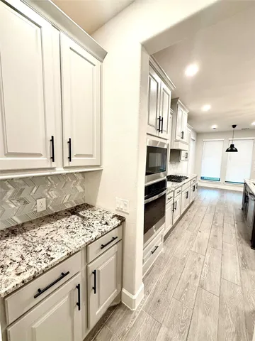 a large kitchen with stainless steel appliances kitchen island granite countertop a stove a sink dishwasher and a microwave oven with large wooden cabinets