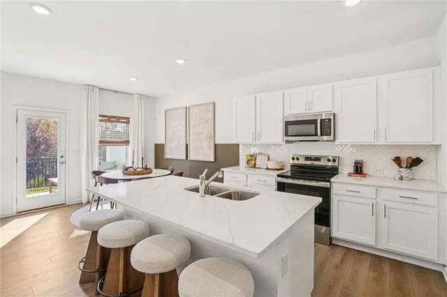 a kitchen with stainless steel appliances a stove a sink dishwasher a refrigerator with white cabinets and wooden floor