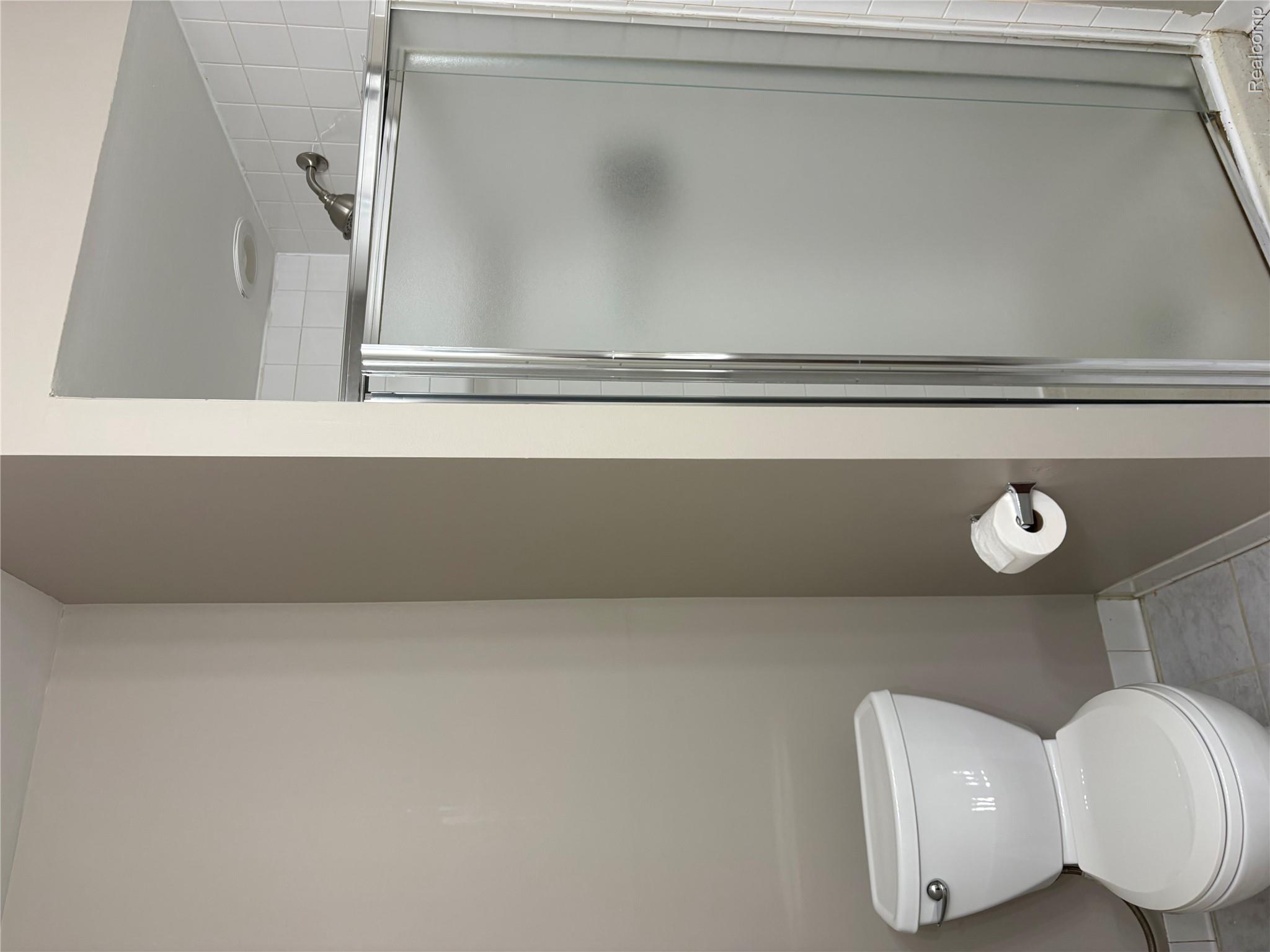 30200 Southfield Road Southfield, MI 48076 - Photo 8 of 14 Walk-in shower with a frosted glass enclosure and a white tiled surround, complemented by a white toilet and light-colored wall paint