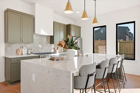 a kitchen with stainless steel appliances a stove a refrigerator a sink a dining table and chairs with wooden floor