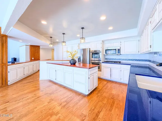 a large kitchen with stainless steel appliances granite countertop a stove top oven a sink dishwasher and white cabinets with wooden floor