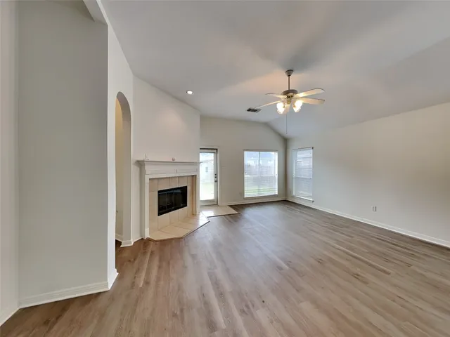 an empty room with wooden floor fireplace fan and windows