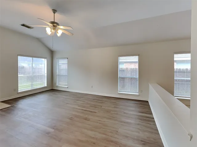 a view of an empty room with wooden floor and fan
