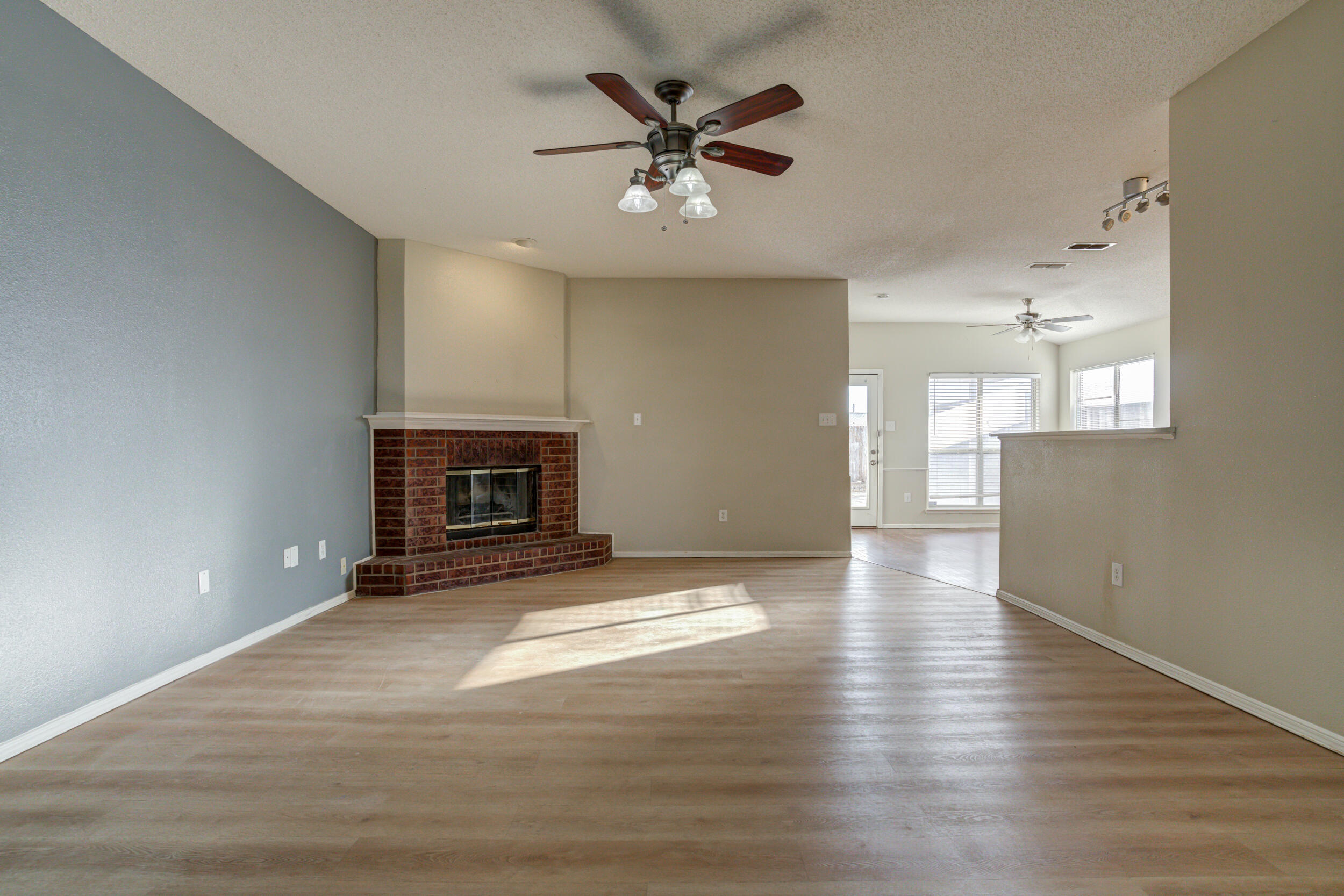 6221 18th Street Lubbock, TX 79416 - Photo 12 of 48 an empty room with wooden floor a ceiling fan a fireplace and windows