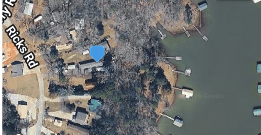 An aerial perspective shows the property situated near the water with surrounding mature trees.