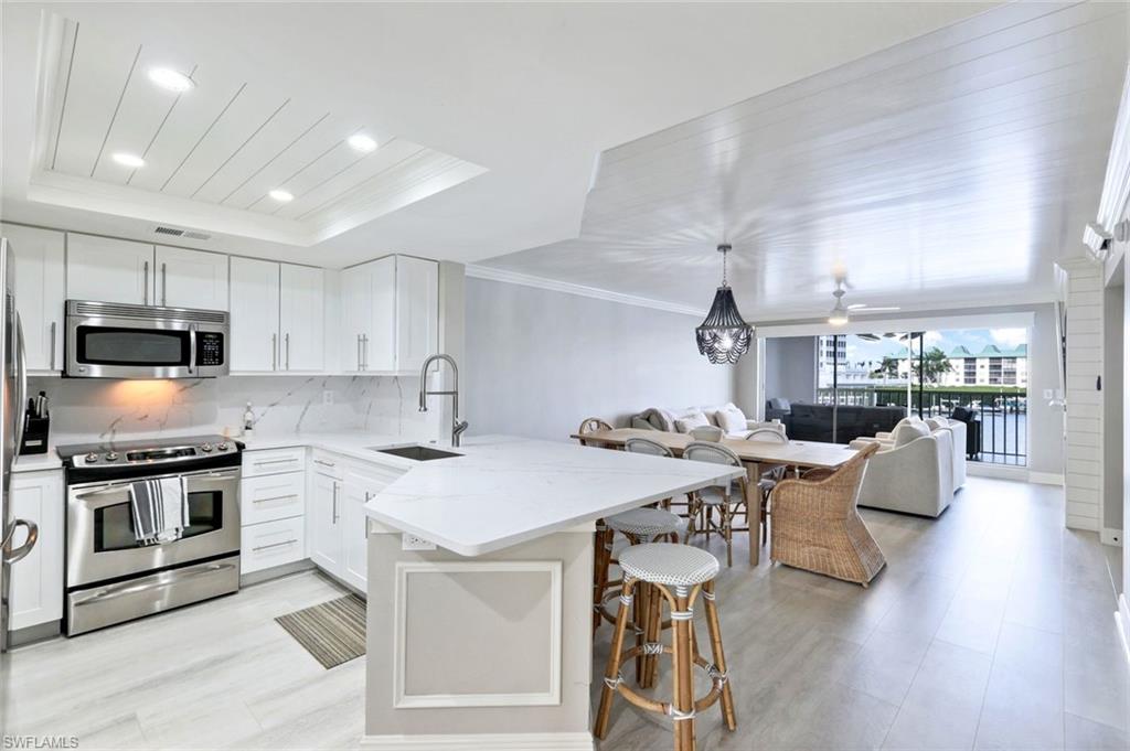 9103 Vanderbilt Drive, Unit 208 Naples, FL 34108 - Photo 4 of 23 a open kitchen with stainless steel appliances granite countertop a stove top oven a sink dishwasher a dining table and chairs with wooden floor