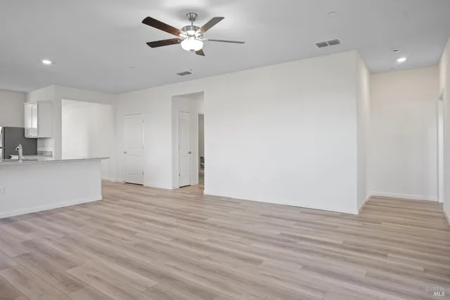 a view of an empty room with wooden floor and a ceiling fan