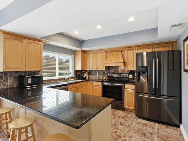 a kitchen with granite countertop a refrigerator a stove a sink a dining table and chairs with wooden floor