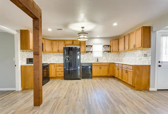 a kitchen with stainless steel appliances kitchen island granite countertop a refrigerator a stove top oven a sink and dishwasher with wooden floor