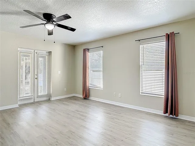 an empty room with wooden floor chandelier fan and windows
