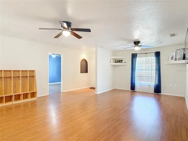 a view of an empty room with wooden floor and a ceiling fan