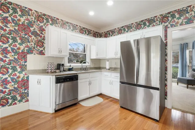 a kitchen with stainless steel appliances granite countertop a refrigerator a stove a sink dishwasher and white cabinets with wooden floor