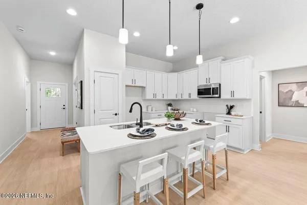 a kitchen with stainless steel appliances kitchen island granite countertop a sink a stove a refrigerator and white cabinets with wooden floor